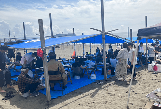 砂浜でブルーシートと日除けを設置し、地引網のレクリエーションに参加する人々
