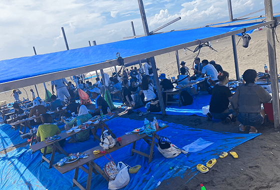 海辺でテーブルを囲みながら、地引網のレクリエーションを楽しむ参加者たち